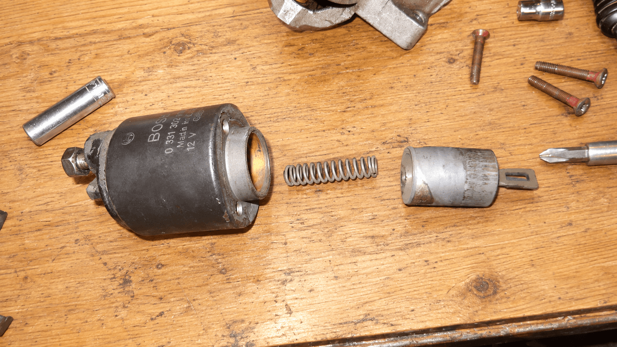 Disassembled starter solenoid with its return spring and plunger on a workbench