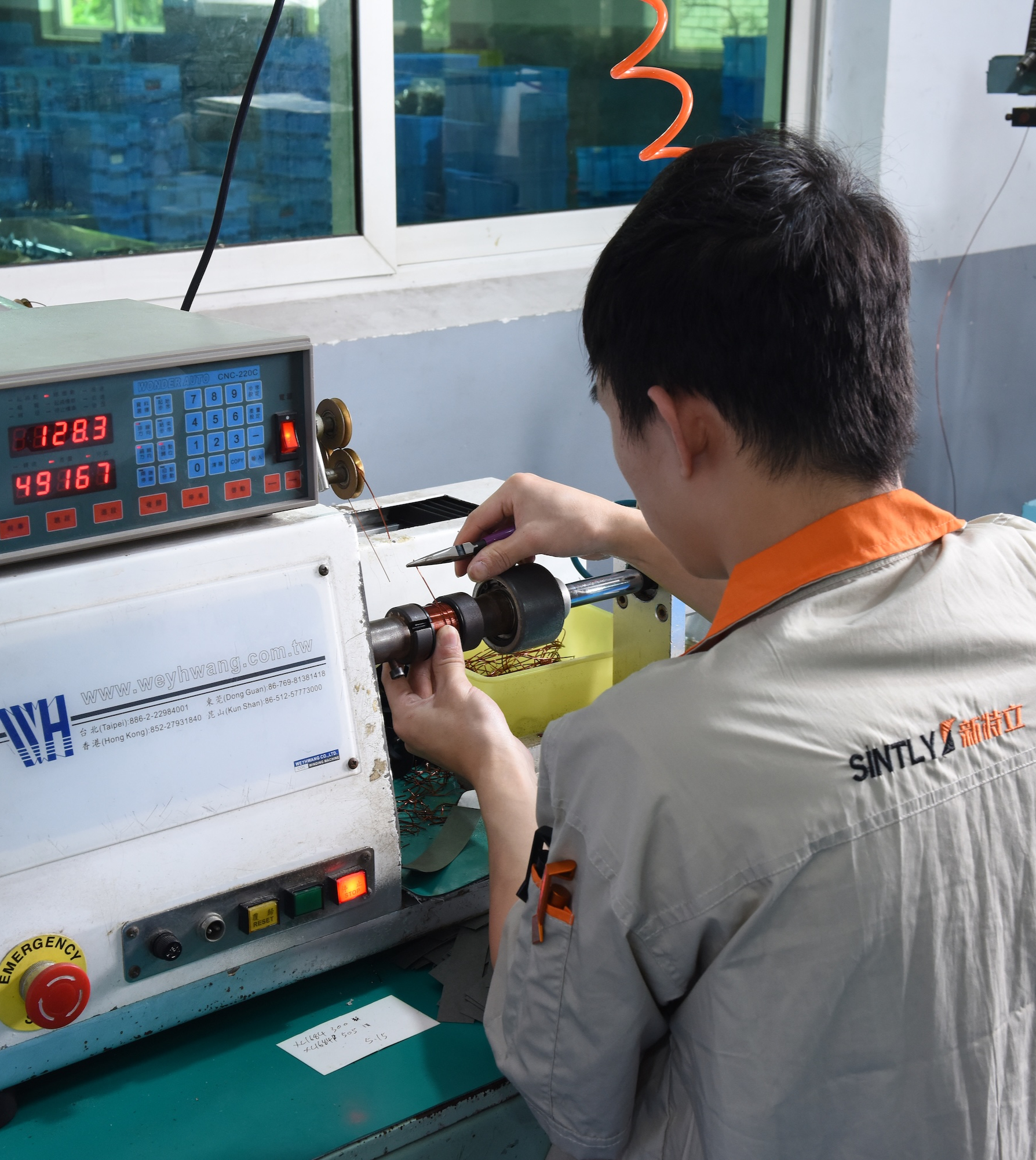 Factory worker operating a coil winding machine for automotive motor components