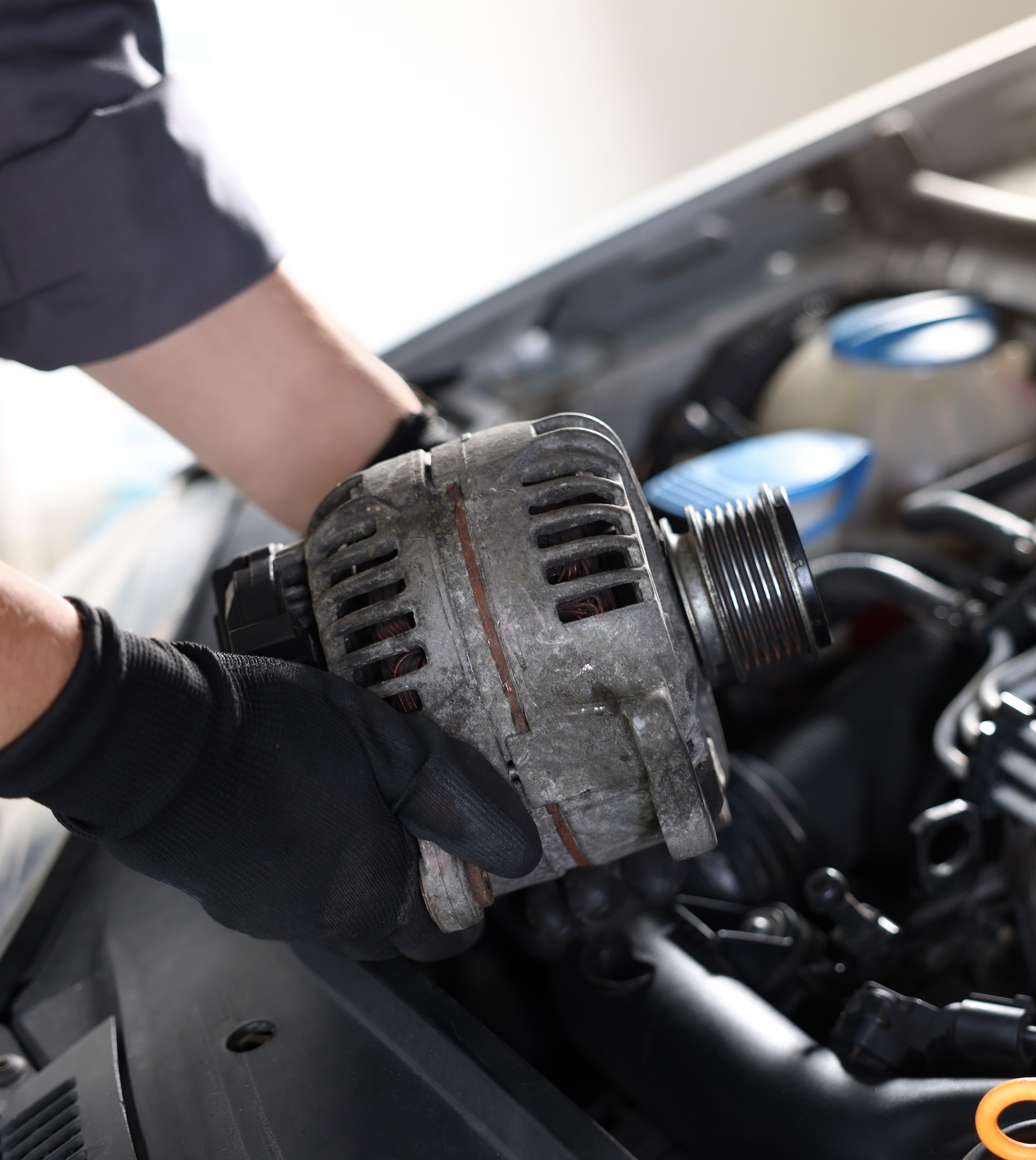 Mechanic removing a used alternator from a car engine bay