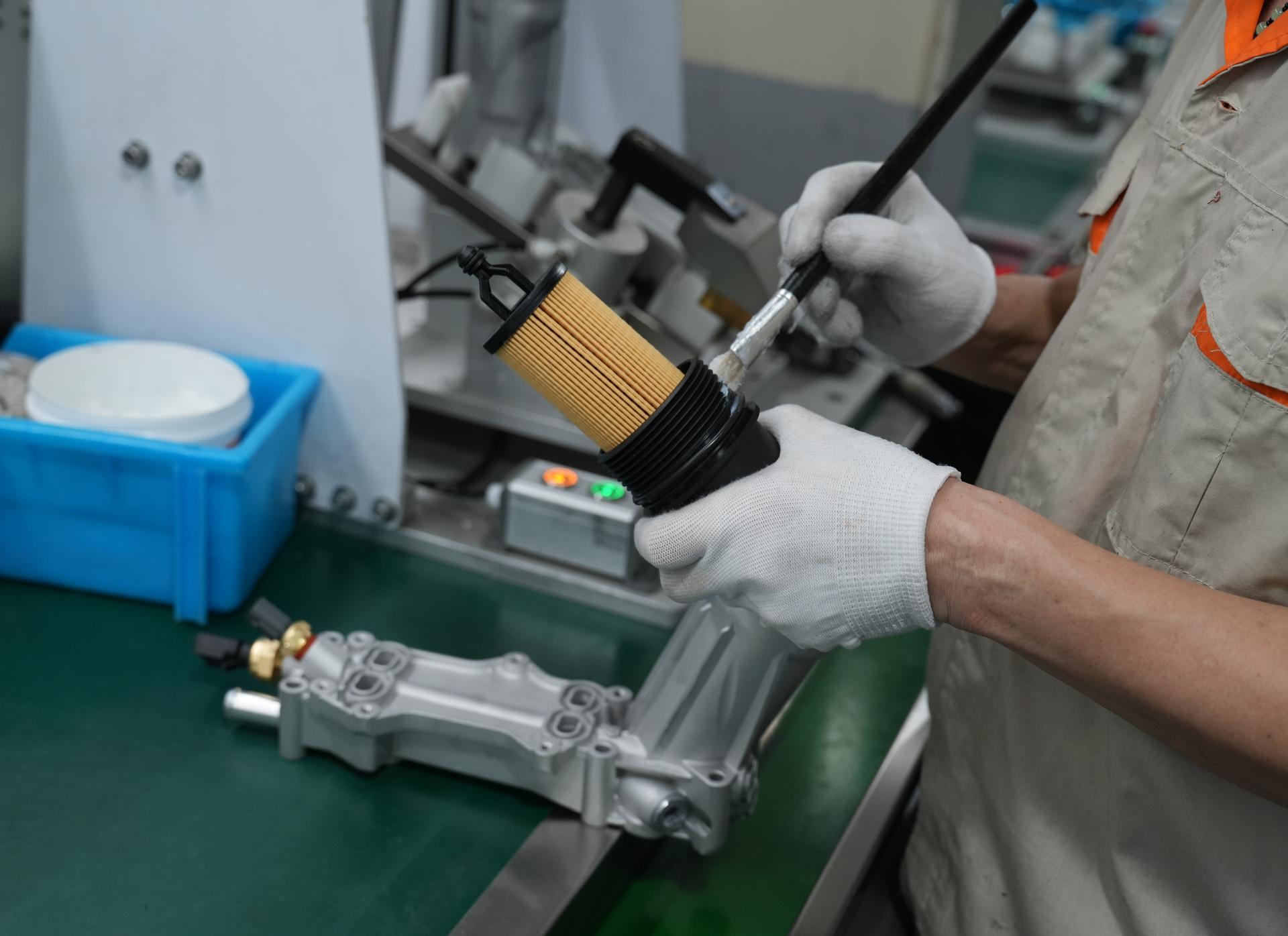 Factory worker applying sealant to a cartridge oil filter cap during assembly