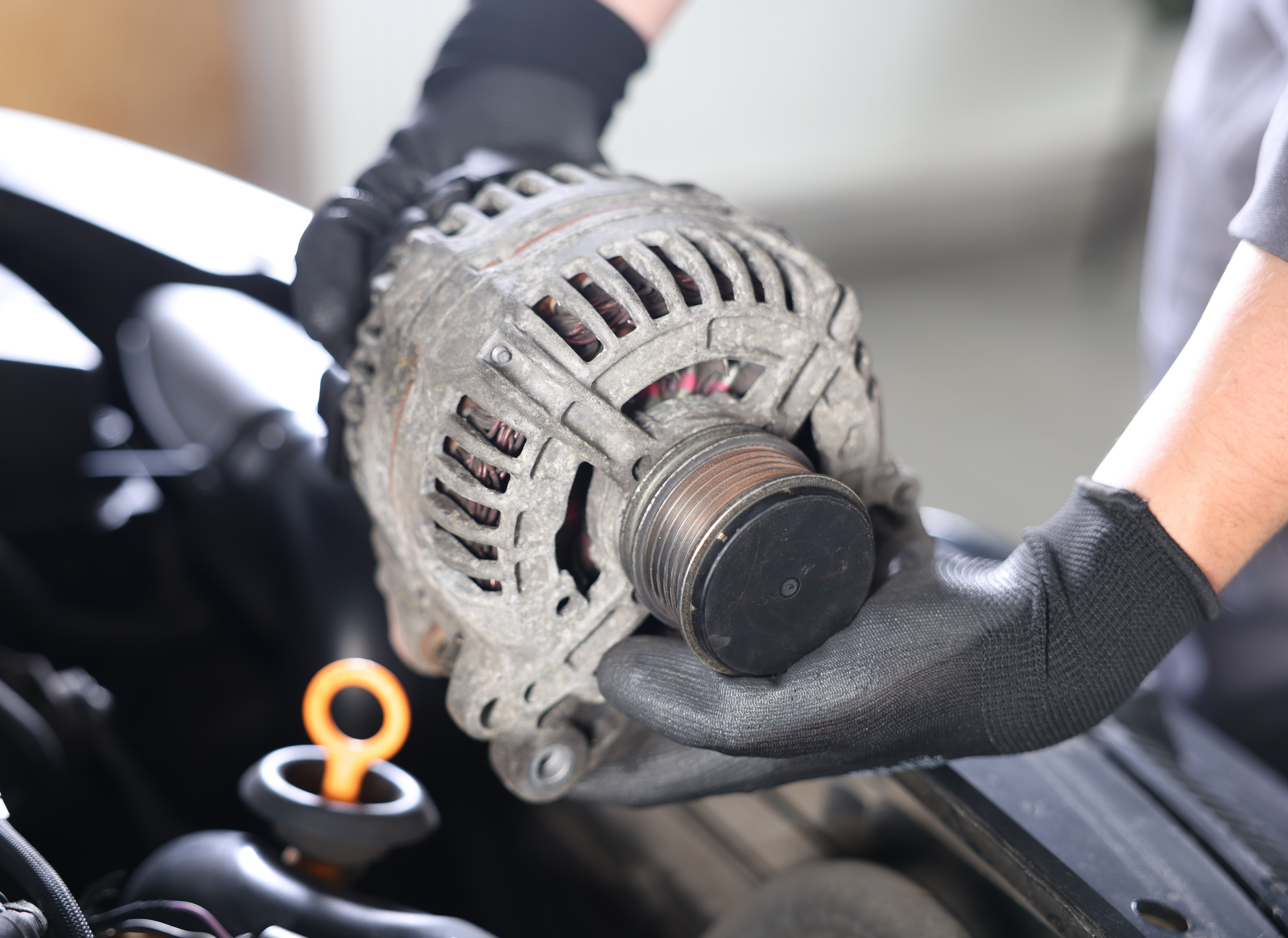 Mechanic holding a removed alternator beside an open car hood