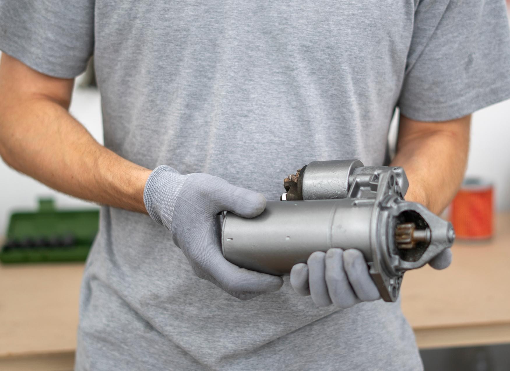 Mechanic holding a car starter motor before installation