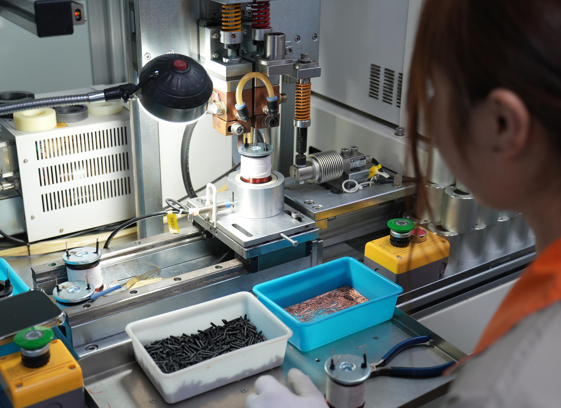 Factory worker operating a machine to assemble copper-wound automotive solenoid coils
