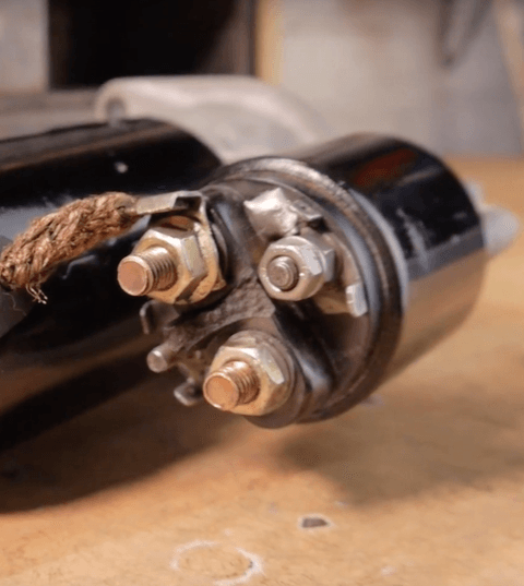 Starter motor with an attached solenoid and copper terminals on a workbench